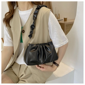 Detail of black glossy cloud bag with ruched shoulder strap worn by a female model