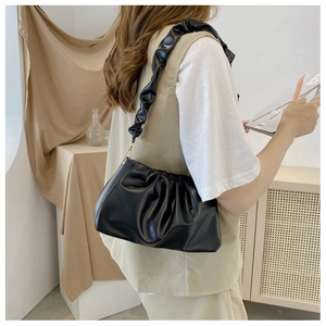Detail of black pleated cloud bag texture with golden metal hooks worn by a model