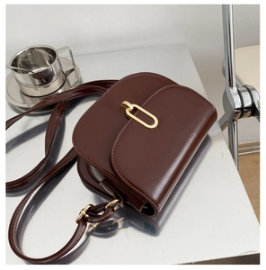 Detail der dunkelbraunen Satteltasche mit goldener U-Schnalle auf poliertem Metall