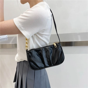 Chic black pleated shoulder bag with gold chain strap shown on a model's arm