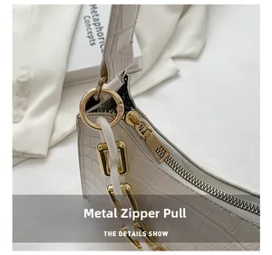 Detail of white crocodile pattern handbag featuring a gold zipper and metal chain