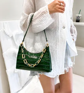 Deep green crocodile pattern handbag with chunky gold chain detail worn by a model