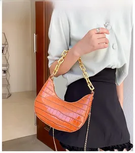 Detail of bright orange faux leather crescent bag with crocodile pattern and chunky gold chains