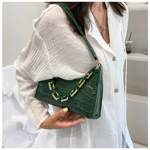 Detail of dark green crocodile pattern shoulder bag with golden chain and thin strap