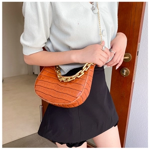Detail of a brown crocodile pattern half-moon bag featuring a thick gold chain and strap