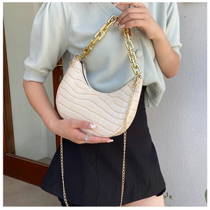 Macro shot of beige crescent bag featuring embossed crocodile pattern and gold chain strap