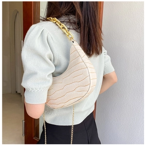 Detail of cream crocodile pattern crescent bag with chunky gold chain strap on shoulder