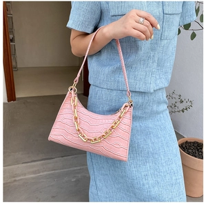 Macro detail of pink crocodile pattern leather and gold chain on crescent shoulder bag