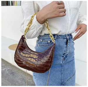 Detail of brown crocodile embossed hobo bag with thick gold chain strap and polished finish