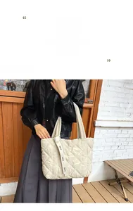 Detail of beige quilted tote bag with lettered decorative strap for autumn and winter