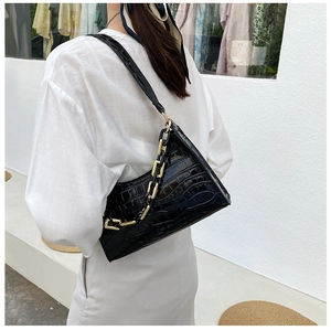 Detail of black crocodile texture shoulder bag featuring chic gold and black chain link