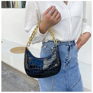 Detail of black crocodile texture crescent bag with chunky gold chain strap on a model