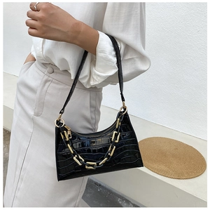 Detail of black crocodile texture baguette bag with thick gold decorative chain