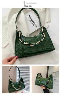 Detail of green crocodile textured handbag with a chunky gold chain strap and glossy finish