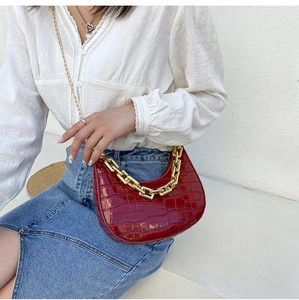Detail of red crocodile pattern crescent bag with chunky gold chain on model
