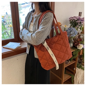 Detail of brick red quilted tote bag with diamond stitching and lettered strap
