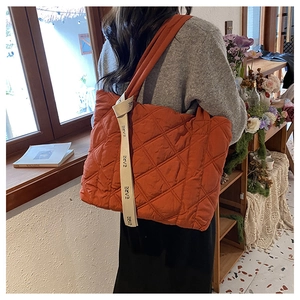 Close-up of rust red quilted tote bag with diamond stitching and decorative logo ribbon