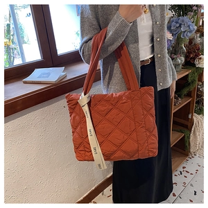 Close-up of orange quilted tote bag with diamond stitching and ribbon handle detail