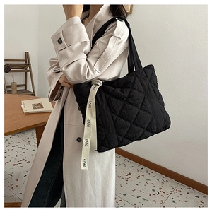 Detail of black quilted tote bag with lettered ribbon strap on beige trench coat