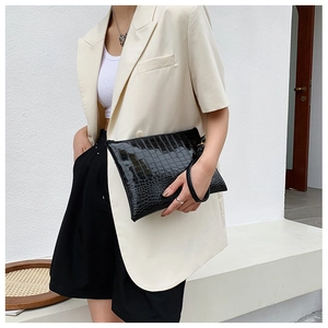Dettaglio di pochette a busta nera con trama a coccodrillo e cinturino da polso alla moda