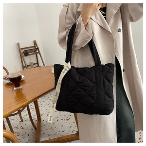 Detailed view of black quilted tote bag featuring a white CARE logo ribbon strap