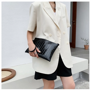 Dettaglio di una pochette nera da donna con trama a coccodrillo e cinturino a cerchio