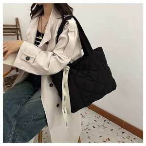 Detail of black quilted tote bag featuring a decorative cream lettered ribbon strap