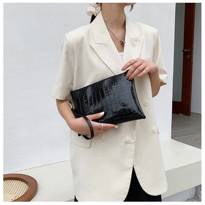 Dettaglio della pochette nera con trama a coccodrillo, fibbia dorata e cinturino elegante