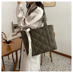 Detail of olive green quilted tote bag showing diamond stitching and logo webbing strap