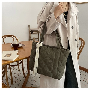 Detail of army green quilted tote bag with EARE strap shown on a beige trench coat