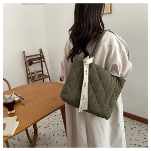 Detail of olive green quilted tote bag with a white ribbon featuring CARE lettering