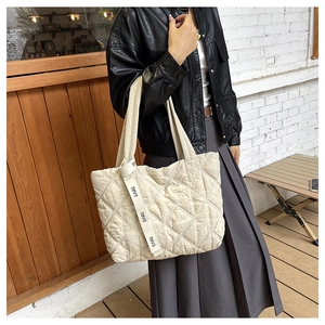 Close-up of beige quilted tote bag with diamond stitching and EARE lettered ribbon strap
