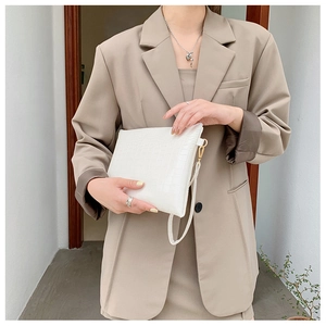 Pochette a busta bianca con motivo a coccodrillo portata da una modella in tailleur