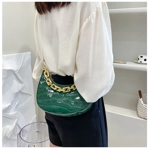 Detail of green crocodile texture crescent bag with chunky gold chain strap worn by a model