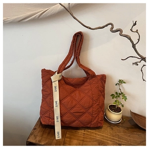 Close-up of rust-red quilted cotton tote bag with decorative EARE ribbon on a wooden surface