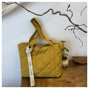 Detail of mustard yellow quilted tote bag with diamond pattern and lettered strap