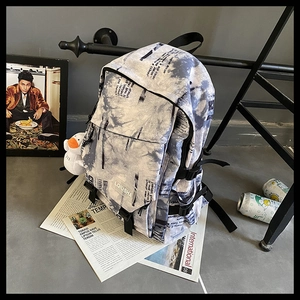 Détail d'un sac à dos style urbain avec motif tie-dye, imprimé journal et pendentif