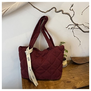 Close-up of burgundy quilted tote bag featuring a soft padded texture and CARE printed strap