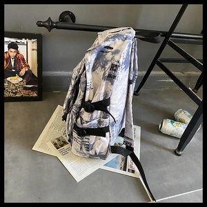 Détail du côté du sac à dos montrant l'imprimé journal, la boucle et la toile robuste