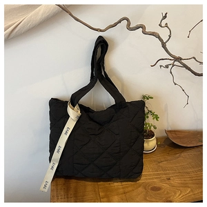 Macro detail of black quilted tote bag with white EARE ribbon handle and minimalist design