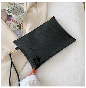 Dettaglio pochette a busta nera con trama a coccodrillo, zip dorata e cinturino da polso
