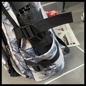 Détail de la poche latérale avec parapluie et boucle réglable sur le sac à dos imprimé journal