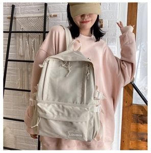 Detail of beige high-capacity school backpack featuring minimalist front pocket and brand tag