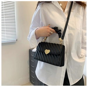 Detail of black quilted handbag with heart-shaped gold clasp and ruched fabric handle