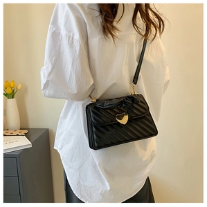 Detalle de bolso negro bandolera con cierre de corazón dorado y asa plisada de moda