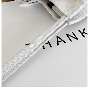 Detail shot of reinforced stitching and fine canvas texture on white tote bag handles