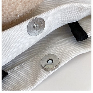 Macro shot of silver magnetic buckle and black webbing on a white canvas bag