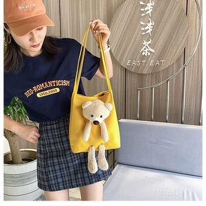 Detail of yellow canvas tote with a 3D plush bear design worn as a crossbody bag
