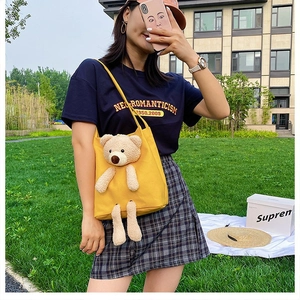 Detail of yellow canvas bag featuring a 3D plush bear ornament worn by a model outdoors