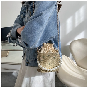 Detail of woven straw bucket bag featuring pearl handle and pink floral embroidery